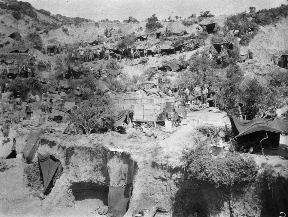 No 1 Outpost. The covers to the entrances of dugout shelters can be seen along the hillside terraces. Soldiers are lined up in front of the dugouts. 